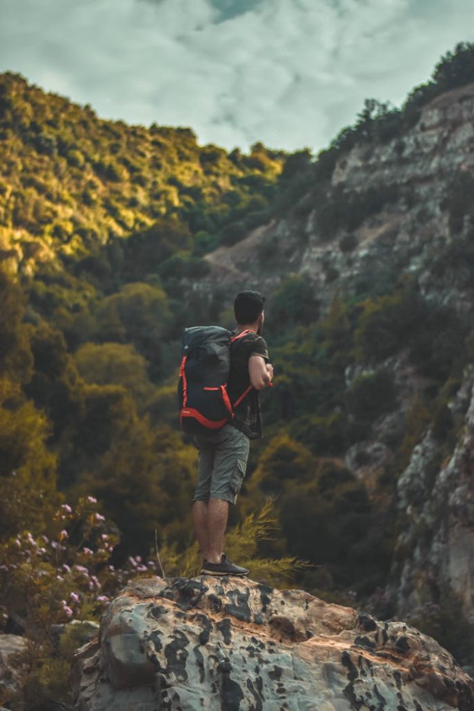 Hiker with a Husqvarna Xplorer backpack standing on a rock overlooking a scenic trail, ideal for adventure travel and outdoor activities.